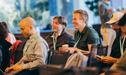 Attendees laughing and smiling while seated in an audience during a conference session.