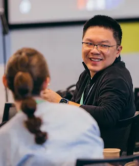 A smiling man wearing glasses looking toward a colleague during a meeting.
