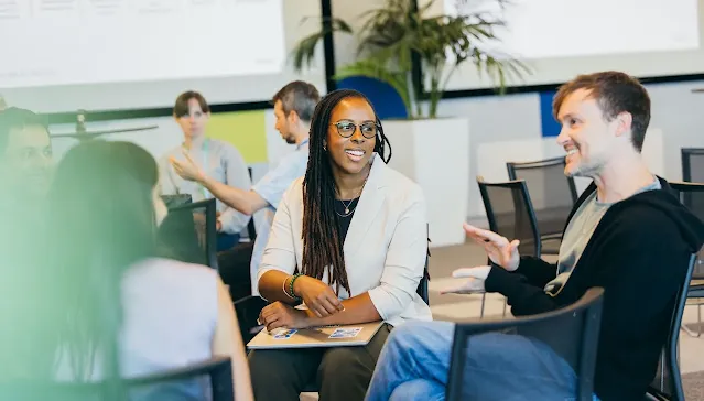 A smiling woman listening to a male colleague during a casual office meeting.