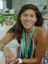 A woman smiling while sitting on a chair with her elbow on the table.