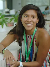 A woman smiling while sitting on a chair with her elbow on the table.